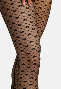 Nohy oblečené v černých punčochách z rybí sítě s vzorem malých a středních černých srdcí, ruka spočívající na horní stehně s nehtovým uměním v podobě srdíček.