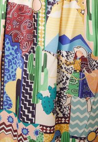 Tissu multicolore à motifs comprenant des cactus, des montagnes, et une silhouette vêtue d'une robe détaillée avec diverses textures et motifs géométriques.