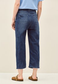 Vaqueros cortos de color azul oscuro con un ajuste relajado, con bolsillos traseros y una textura suave. Combinados con zapatos marrones sin cordones.