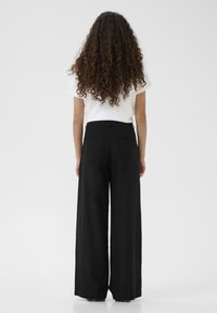 Pantaloni larghi neri realizzati in un tessuto morbido e testurizzato, con vita alta e tasche posteriori per un design minimalista.