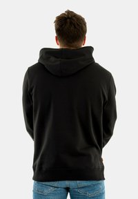 Zwarte hoodie met een trekkoordcapuchon, ribgebreide manchetten en onderkant. Heeft een eenvoudig ontwerp en een zachte stof. Draagt met blauwe jeans.