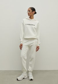 Krémová súprava mikiny a teplákov s logom "LAMANIA". Hladká tkanina, voľný strih, rebrované manžety a štýlové tenisky.