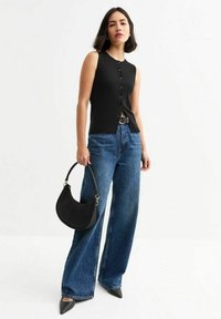 Zwarte geribbelde gebreide tanktop met knopen aan de voorkant, gecombineerd met hoog-taille wijdvallende blauwe jeans en een zwarte halvemaanvormige handtas.