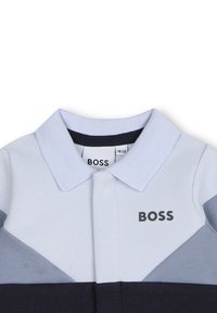 Polo en bleu clair avec un motif texturé, doté d'un col bleu marine, d'un design triangulaire et d'une broderie de logo noire sur la poitrine.