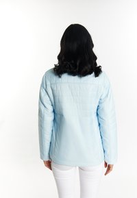 Jachetă puffy de culoare albastru deschis, cu un design ajustat, având o textură netedă și un spate drept. Asortată cu pantaloni albi.