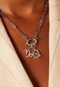Zilveren ketting met een grote ovale schakel, twee hangers: eentje met een rhinestone "n" en de ander een decoratieve "O."