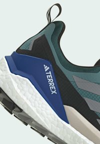 Terrex footwear features a black and teal mesh upper, blue accent, textured grey overlays, and a white cushioned sole with black traction lugs.