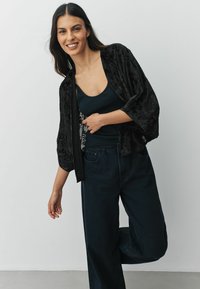Black, sheer kimono-style cardigan with floral texture, worn over a dark tank top and paired with high-waisted dark denim pants.