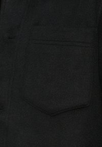 Sort uldfrakke med en forlommet og en blød, tekstureret overflade. Enkel design med rene linjer.