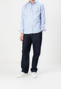 Jasnoniebieska koszula w paski z długimi rękawami, z kołnierzykiem zapinanym na guziki; zestawiona z luźnymi, ciemnymi dżinsami i białymi trampkami.