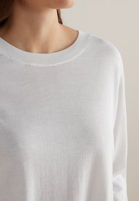 Lekki, biały sweter dzianinowy z okrągłym dekoltem i długimi rękawami, charakteryzujący się gładką teksturą i żebrowanym wykończeniem przy dekolcie.
