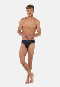 Slip neri con un design semplice, caratterizzati da un elastico discreto. Il modello assume una posa neutra, esibendo la texture e la vestibilità del tessuto.