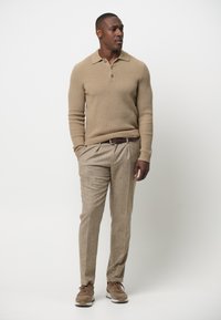 Beige gerippter Pullover mit drei Knöpfen, kombiniert mit hellbraunen Tweed-Hosen und braunen Turnschuhen. Einfaches und figurbetontes Design.