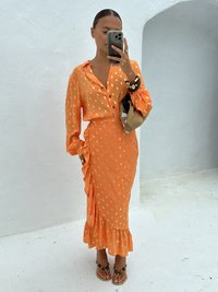 Orange-Kleid mit Polka-Dots, mit Knopfverschluss vorne, gerafftem Saum und taillierter Silhouette. Getragen mit Perlen-Sandalen und einer gewebten Tasche.