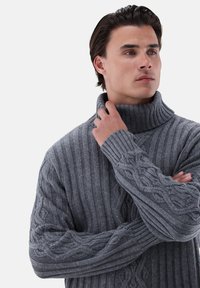 Grauer Strickpullover mit hohem Kragen, der über Ripp- und Zopfmuster verfügt. Die Textur ist dick und der Pullover hat lange Ärmel und eine lockere Passform.