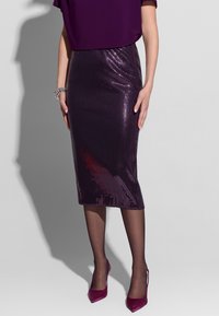 Fioletowa spódnica ołówkowa z cekinów o dopasowanym fasonie, sięgająca do połowy łydki, o gładkiej fakturze, uzupełniona przez przezroczyste rajstopy i pasujące szpilki.