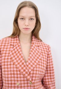 Dwurzędowa marynarka w różowo-pomarańczową kratkę. Cechy szczególne to złote guziki oraz wyrazisty design klap.
