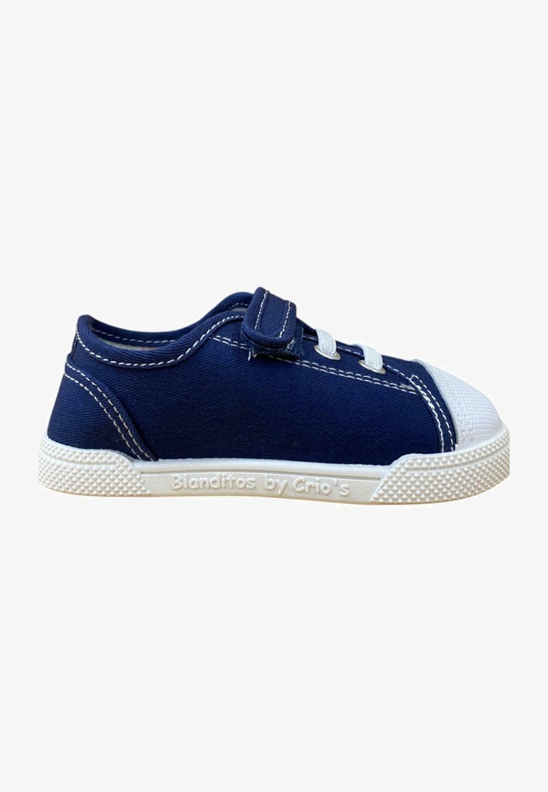 Zapatilla de lona en color azul marino con puntera de goma blanca y suela texturizada. Cuenta con cordones elásticos y una correa de velcro para ajuste. Logo de la marca en el lateral.
