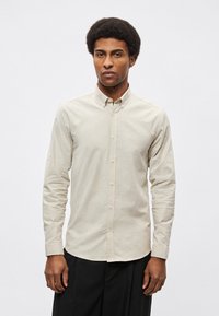 Φωτεινό μπεζ πουκάμισο με μακριά μανίκια και κουμπιά, με μυτερό γιακά, ίσια βάση και εφαρμοστά μανίκια. Κατασκευασμένο από απαλό βαμβακερό ύφασμα.