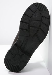 Černá pryžová podrážka boty s texturovaným povrchem, obsahující vzor běhounu pro lepší přilnavost, otisk značky a jemné zvýrazněné detaily.