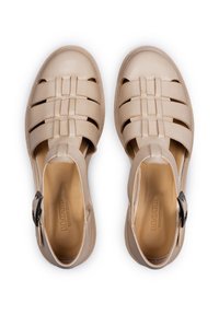 Sandali in pelle beige con un design intrecciato, aperti sulla punta e sul retro, con un accento in nero sulla fibbia della cinghia alla caviglia. Texture liscia e suola piatta.