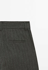 Pantalon sur mesure à fines rayures grises avec une poche passepoilée à l'arrière et des passants pour ceinture sur fond blanc.