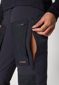 Donkere G-1000 stof broek met ritssluiting zakken. Close-up van een hand die de zijzak opent, waarbij textuur en ontwerpdetails worden benadrukt.