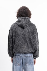 Pessoa com cabelo encaracolado vestindo um hoodie preto lavado e jeans claros soltos, de costas numa fundo branco.