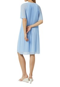 Hellblaues Plissee-Kleid mit kurzen Ärmeln und rundem Ausschnitt, kombiniert mit weißen Keilsandaletten, von hinten gesehen.