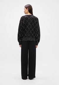 Black knitted sweater with a diamond pattern, featuring sparkling accents and ribbed hem, paired with loose-fitting black trousers.