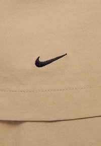 Camisa de tecido bege com um logótipo da Nike bordado em preto na parte da frente. Textura suave, com decote redondo e design de mangas dobradas.