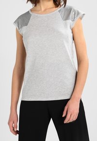 Grå kortärmad topp med en mjuk textur, med glänsande silvermetallicdetaljer på axelpanelerna och en avslappnad passform.