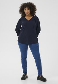 Marineblaues V-Ausschnitt-Bluse mit langen Ärmeln und subtiler Textur, kombiniert mit blauen Skinny-Jeans und schwarzen Plateauschuhen.