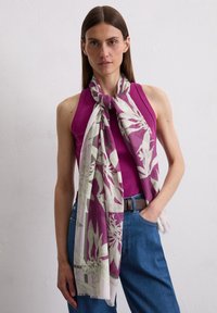 Purple floral scarf with green accents, lightweight fabric, draped around neck, contrasting with a fitted purple top and blue jeans.