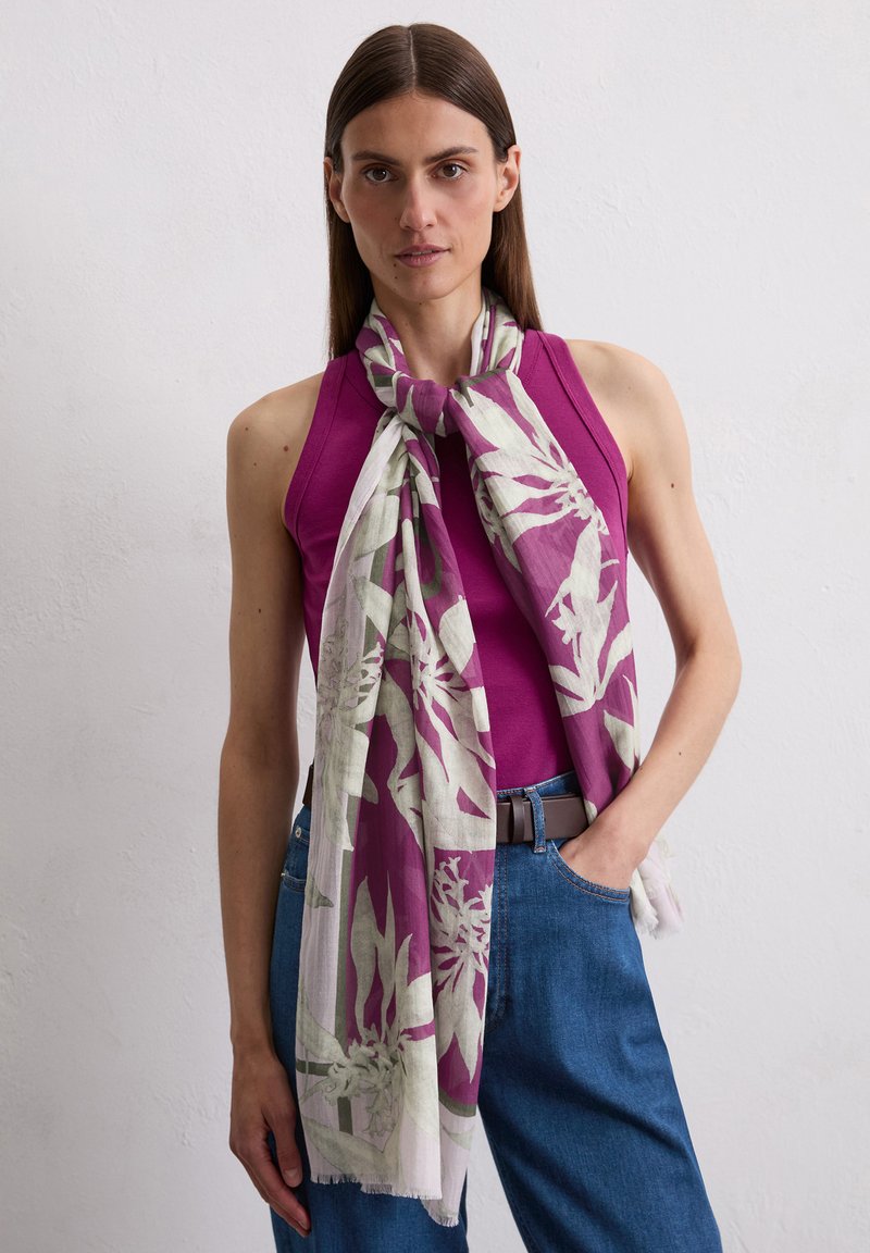 Purple floral scarf with green accents, lightweight fabric, draped around neck, contrasting with a fitted purple top and blue jeans.