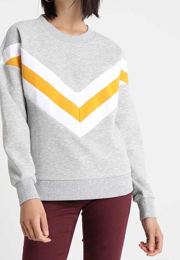 Grijze sweatshirt met een chevronpatroon in wit en geel. Heeft ribgebreide manchetten en een ronde hals. Materiaal lijkt zacht en gestructureerd.
