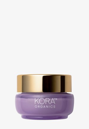 Bocal en verre violet avec couvercle doré, présentant "KORA ORGANICS" en texte blanc sur le devant. Surface lisse, forme ronde, design compact.