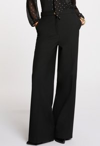 Pantalons larges noirs en tissu lisse, dotés de poches latérales et d'une taille ajustée avec une fermeture à bouton.