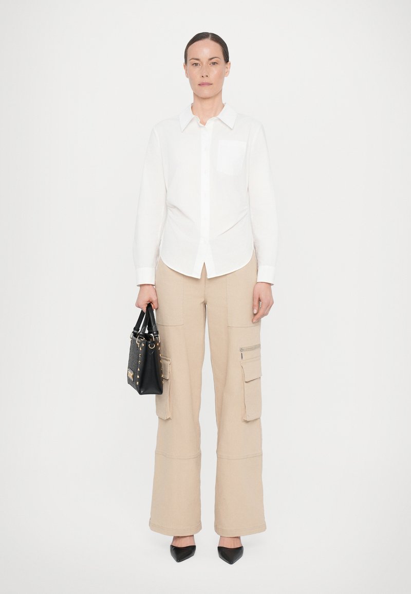 Camisa branca com botão e um bolso no peito, combinada com calças cargo largas bejes. Bolsa preta com superfície texturizada e detalhes em dourado.