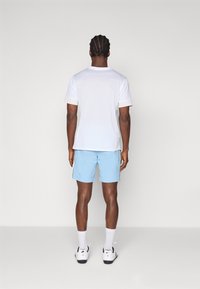 Camisa blanca de manga corta con tejido texturizado, combinada con pantalones cortos azul claro que tienen rayas laterales. Calcetines blancos y zapatos negros completan el conjunto.