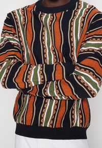 Gestrickter Pullover mit strukturierten Streifen in Orange, Grün und Marineblau, akzentuiert mit Weiß und komplizierten Blumenmustern entlang der Nähte.