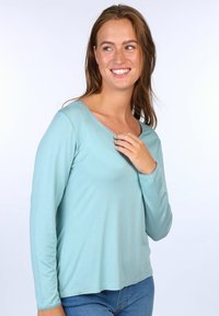 Hellblaues Langarmoberteil mit einem runden Ausschnitt, das entlang der Kanten mit einer spitzenartigen Verzierung versehen ist. Weicher Stoff mit lockerer Passform.