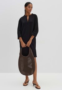 Black oversized dress with a V-neck and three-quarter sleeves, paired with a brown mesh tote bag and strappy black sandals.