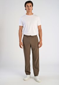 Braune elastische Hosen mit einem Kordelzug, kombiniert mit einem schlichten weißen T-Shirt und weißen Turnschuhen. Einfaches, lässiges Design.