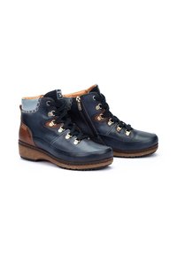 Botas de cuero marinas hasta el tobillo con herrajes dorados, diseño de cordones y cremallera lateral, suela de corcho y acentos marrones contrastantes en el talón.