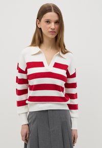 Rot-weißer gestreifter Pullover mit V-Ausschnitt und Kragen, aus weichem Stoff, getragen mit einem gefalteten grauen Rock.