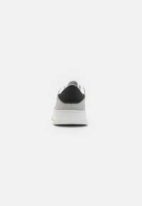 Vista posteriore di una sneaker grigia con suola bianca e accentuazione nera sul tallone. Upper in pelle liscia con design minimalista e forma arrotondata.