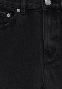 Tissu en denim noir montrant la partie supérieure avant avec bouton en métal, rivets, boucle de ceinture et détails de couture sur un jean.