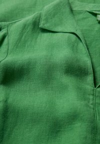 Cămașă verde din in cu guler, având un material texturat și o croială ușor relaxată. Suprafață netedă cu un luciu subtil și detalii împletite.