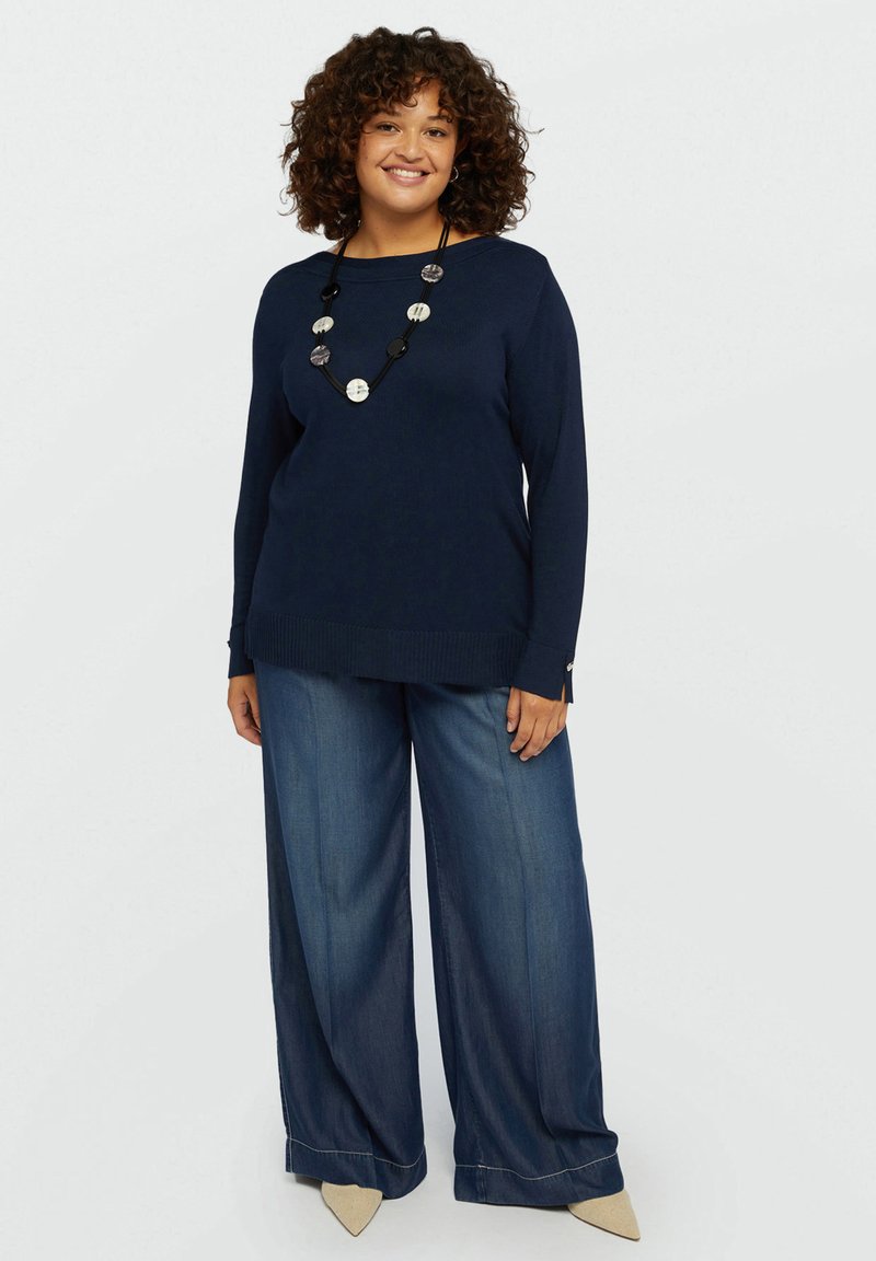 Pull en tricot marine à manches longues, avec des poignets et un ourlet côtelés, associé à un pantalon en denim à jambes larges. Accessoirisé avec un collier de perles multicolores.